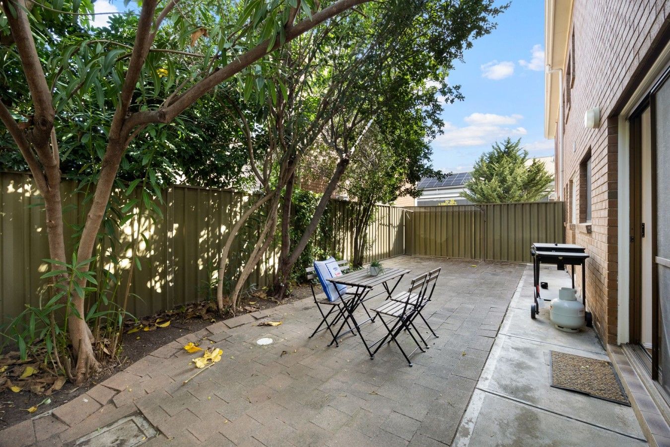 Un jardin avec une terrasse, une table, des chaises, une bouteille de gaz et une clôture.