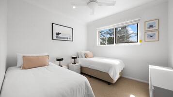 A bedroom with two beds, a ceiling fan, a window with a view, and framed pictures on the wall.
