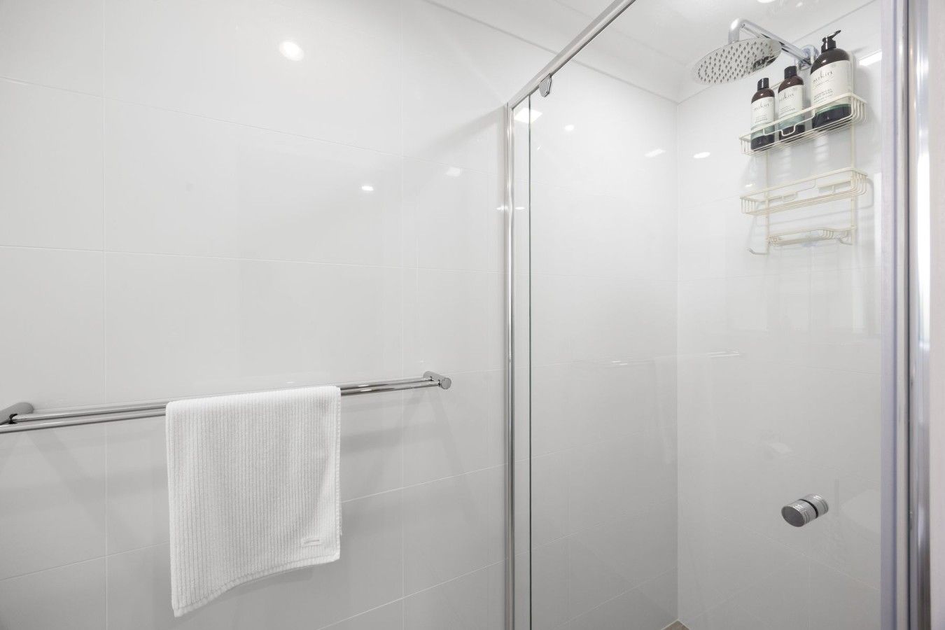 A modern shower with a glass door, a towel rack with a white towel, and a shelf with toiletries.