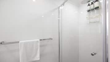 A modern shower with a glass door, a towel rack with a white towel, and a shelf with toiletries.