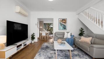 Una sala de estar moderna con una televisión de pantalla plana, un sofá, una mesa de centro y una escalera.