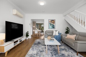 Un salon moderne avec un téléviseur à écran plat, un canapé, une table basse et un escalier.