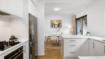 A modern kitchen with white cabinetry, a stainless steel refrigerator, and a dining area with a table and chairs.