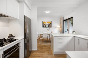 Une cuisine moderne avec des meubles blancs, un réfrigérateur en acier inoxydable et un coin repas comprenant une table et des chaises.