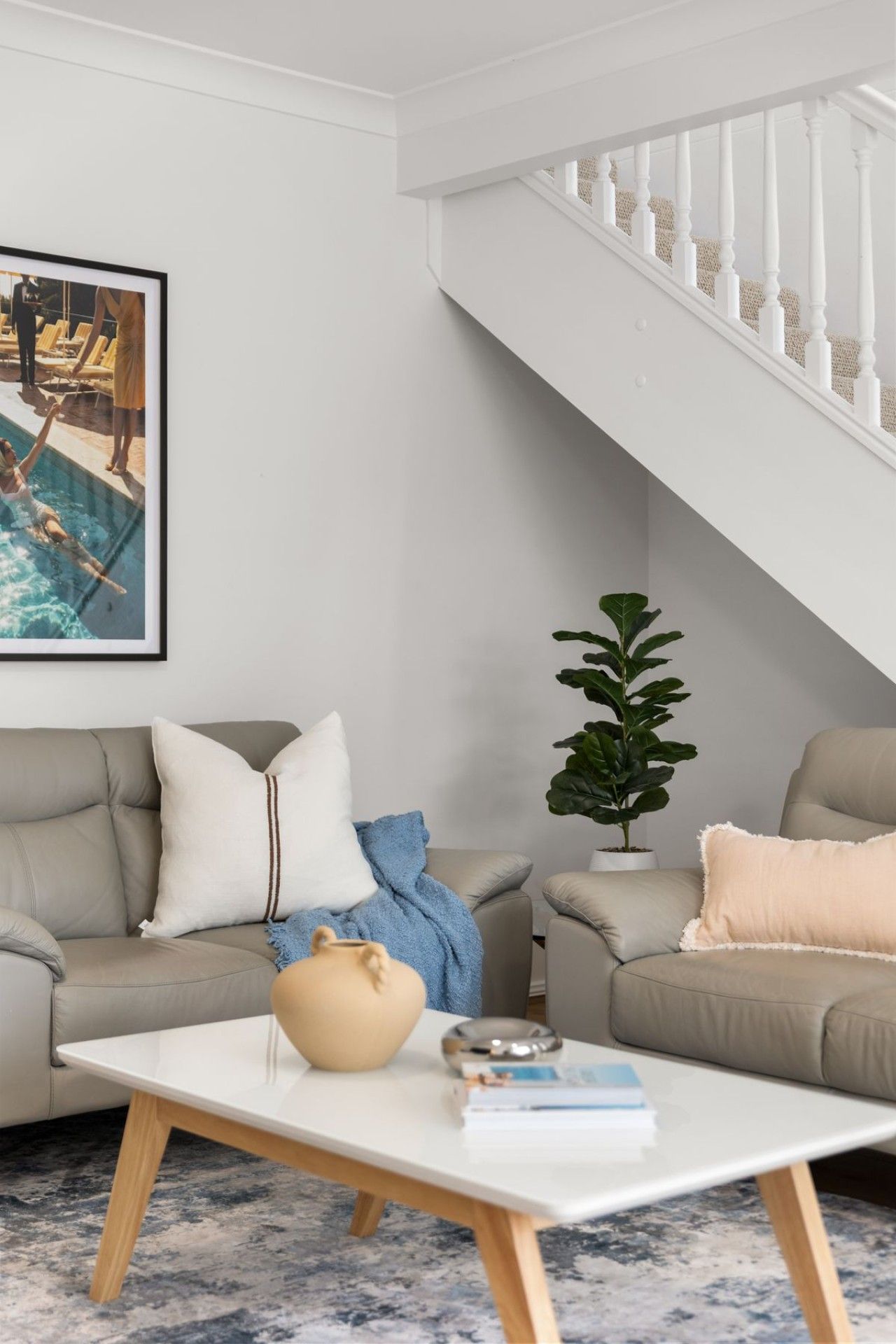A modern living room with a sofa, a coffee table, a potted plant, and a staircase.