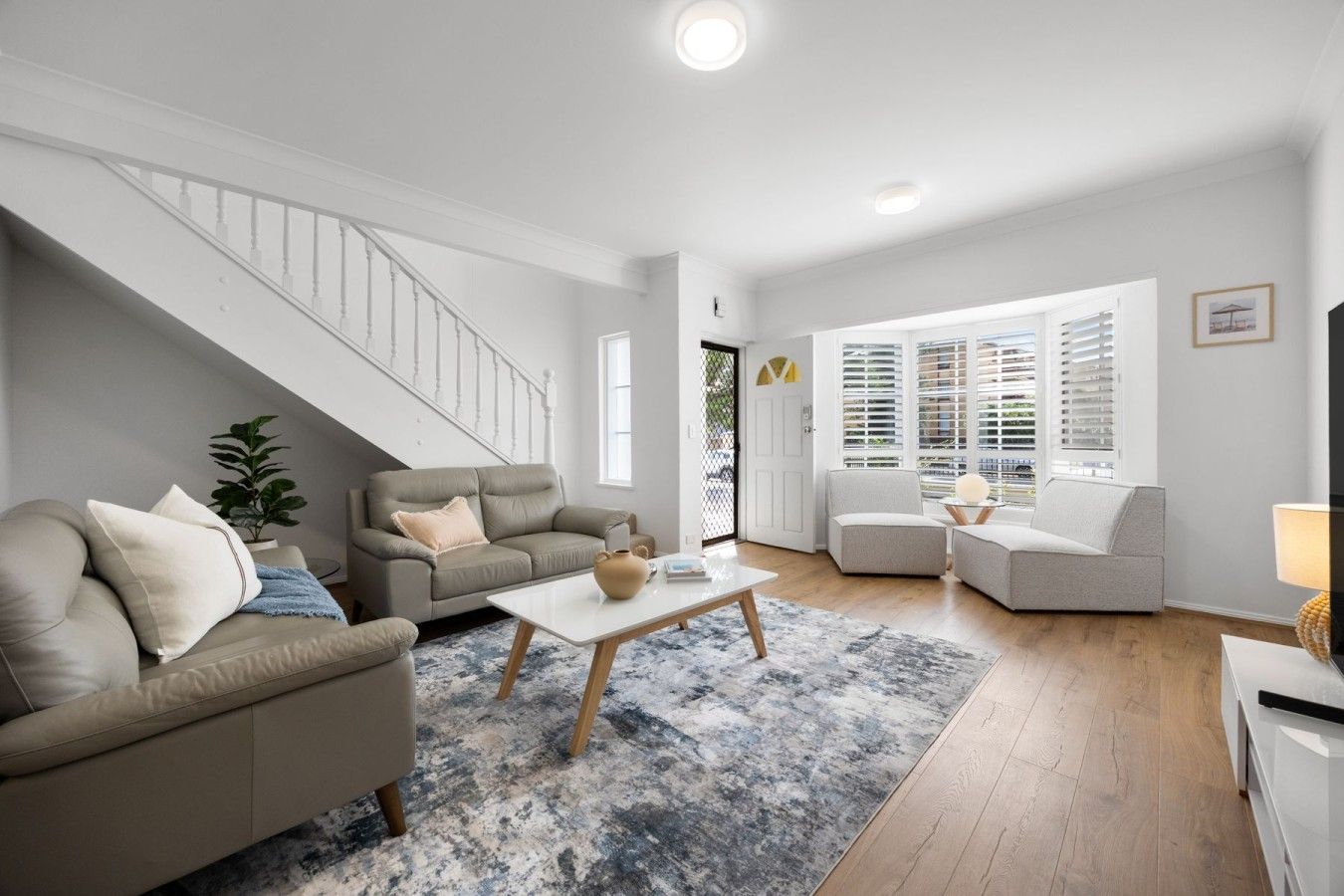 A modern living room with a staircase, two sofas, a coffee table, and a TV.
