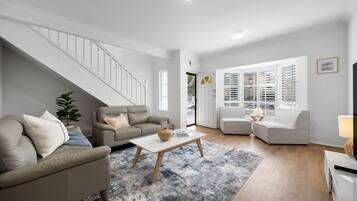 A modern living room with a staircase, two sofas, a coffee table, and a TV.