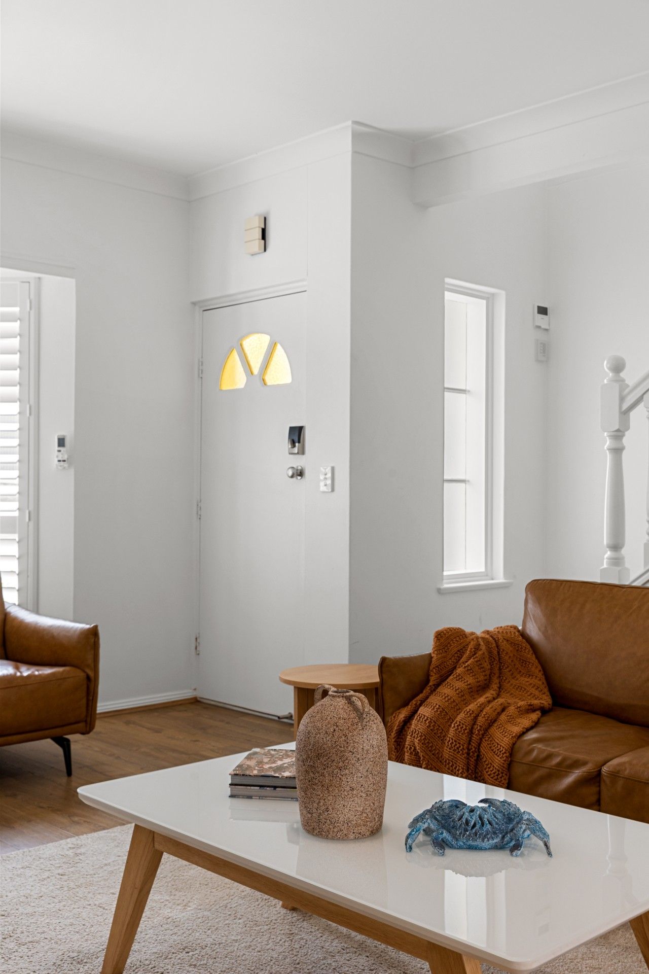 A modern living room with a white coffee table, a brown leather sofa, a brown knitted throw, and a blue sculpture.