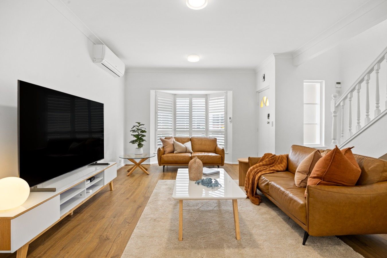 Una sala de estar moderna con un televisor de pantalla plana, sofás de cuero, una mesa de centro y una escalera.