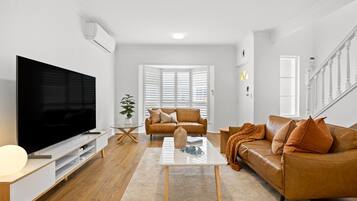 Una sala de estar moderna con un televisor de pantalla plana, sofás de cuero, una mesa de centro y una escalera.