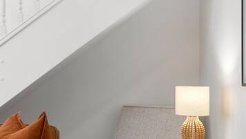 A corner of a room with a staircase, a glass table with a lamp, and a brown leather sofa.