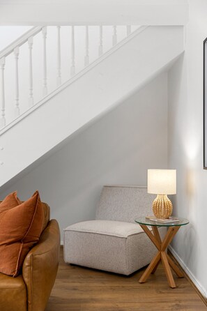 Ein Blick in einen Raum mit einer Treppe, einem Glastisch mit Lampe und einem braunen Ledersofa.