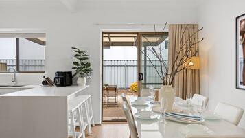A modern kitchen with a central island, a dining area with a table set for two, and a view of the outdoors.
