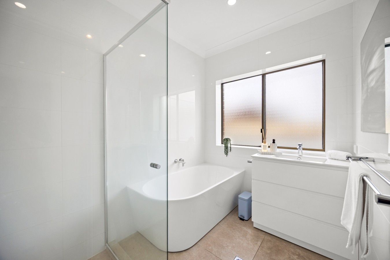 A modern bathroom with a glass shower enclosure, a freestanding bathtub, and a vanity with a window above.