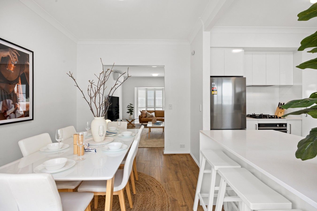 A modern kitchen with white cabinetry, a stainless steel refrigerator, and a dining area with a white table and chairs.
