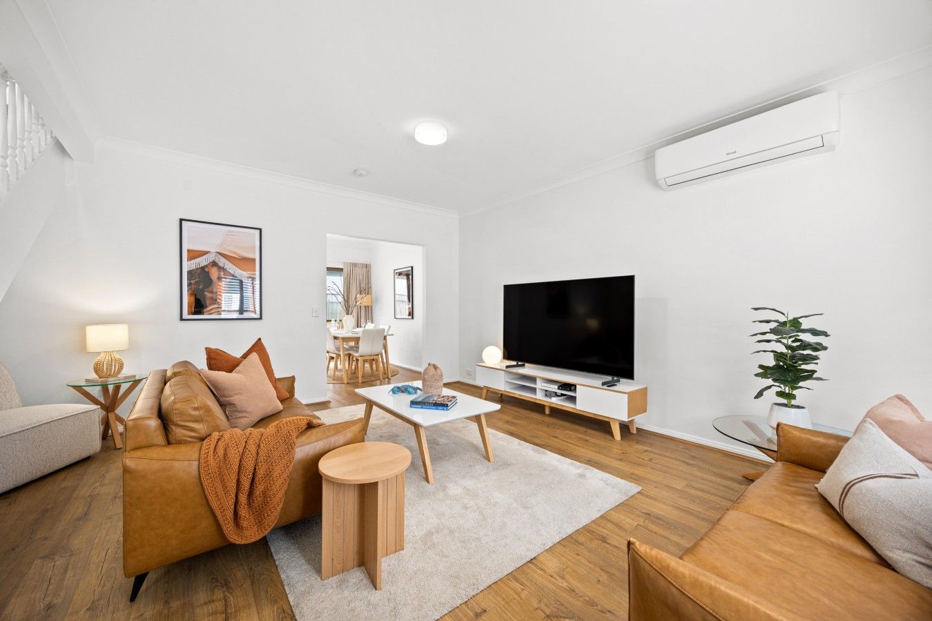 A modern living room with a flat-screen TV, leather sofas, a coffee table, and a potted plant.