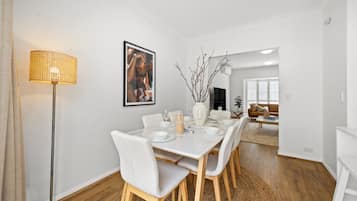 Un coin repas avec une table blanche dressée pour quatre personnes, un lampadaire et un tableau encadré au mur.
