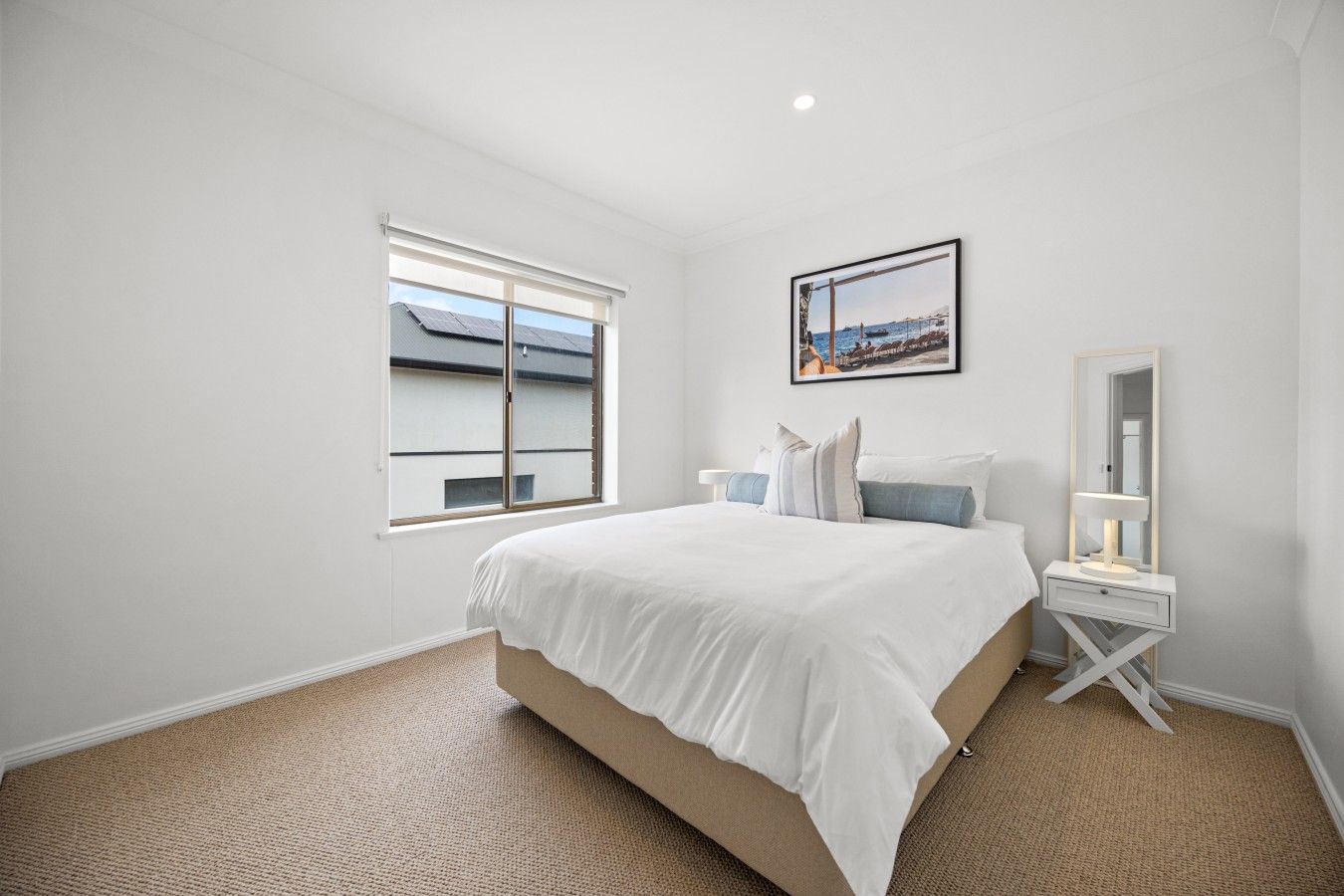 A bedroom with a large bed, a window, a bedside table with a lamp, and a framed picture on the wall.