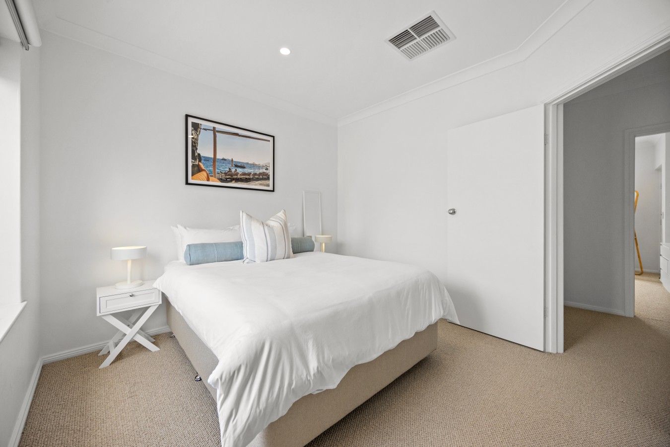 Une chambre à coucher comprenant un lit, des tables de chevet, une commode, un tableau accroché au mur et une porte donnant sur une autre pièce.
