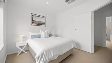 Une chambre à coucher comprenant un lit, des tables de chevet, une commode, un tableau accroché au mur et une porte donnant sur une autre pièce.