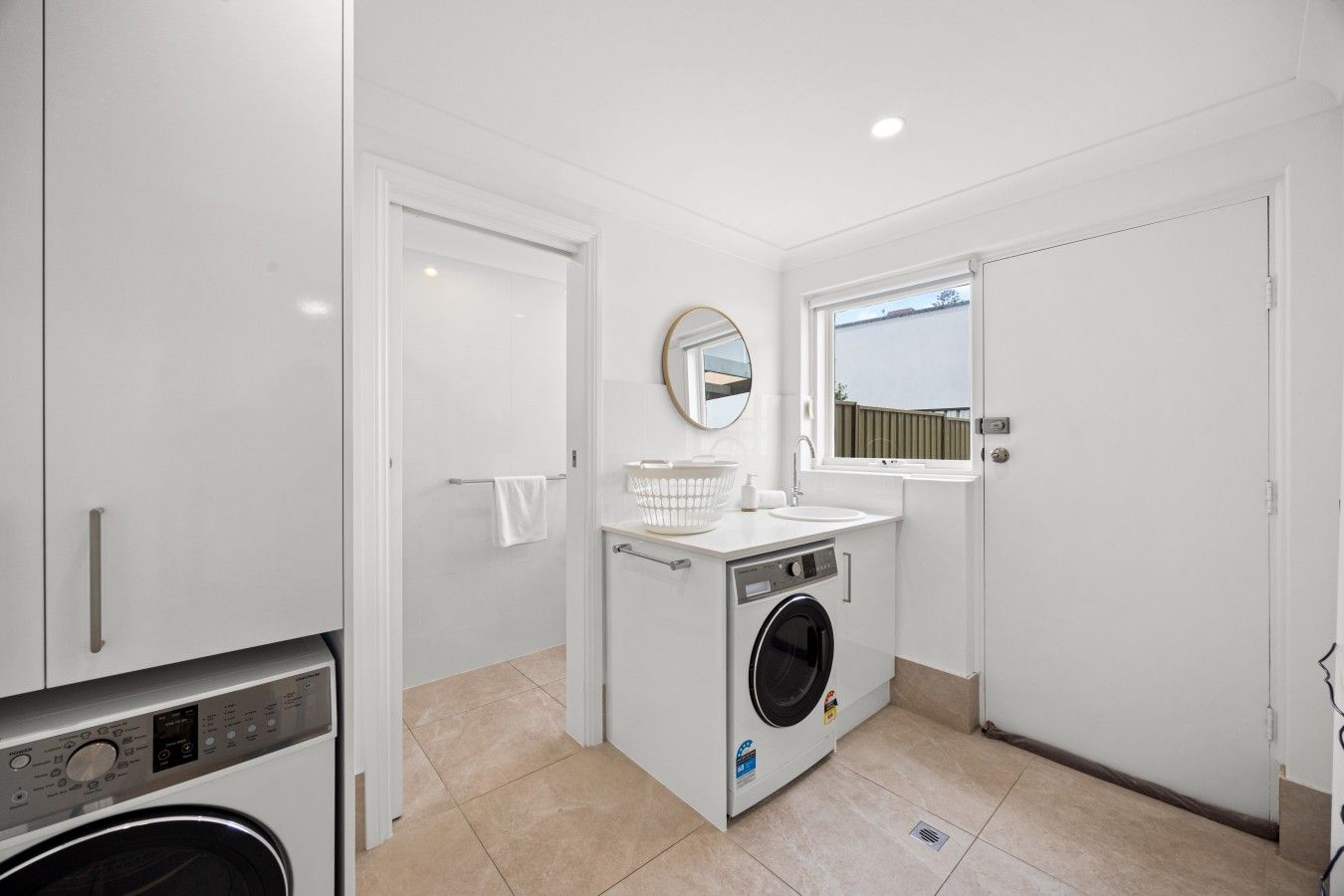 Une petite buanderie équipée d’un lave-linge, d’un évier et d’un miroir.