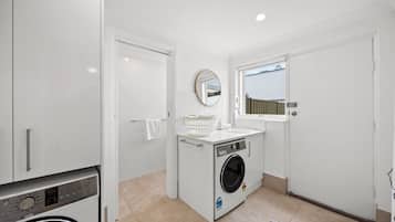 Une petite buanderie équipée d’un lave-linge, d’un évier et d’un miroir.