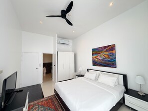 A bedroom with a bed, a desk, a chair, a ceiling fan, an air conditioning unit, a nightstand, a lamp, and a colorful painting on the wall. - A7 - Luxurious 64 sqm Serviced Apartment Near Karon Beach (Tambon Karon)