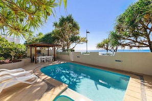 Una piscina con lettini, una zona relax coperta e vista mare.