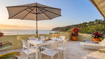 Un espace extérieur aménagé pour prendre les repas, avec une table, des chaises et un parasol, offrant une vue sur un paysage côtier.