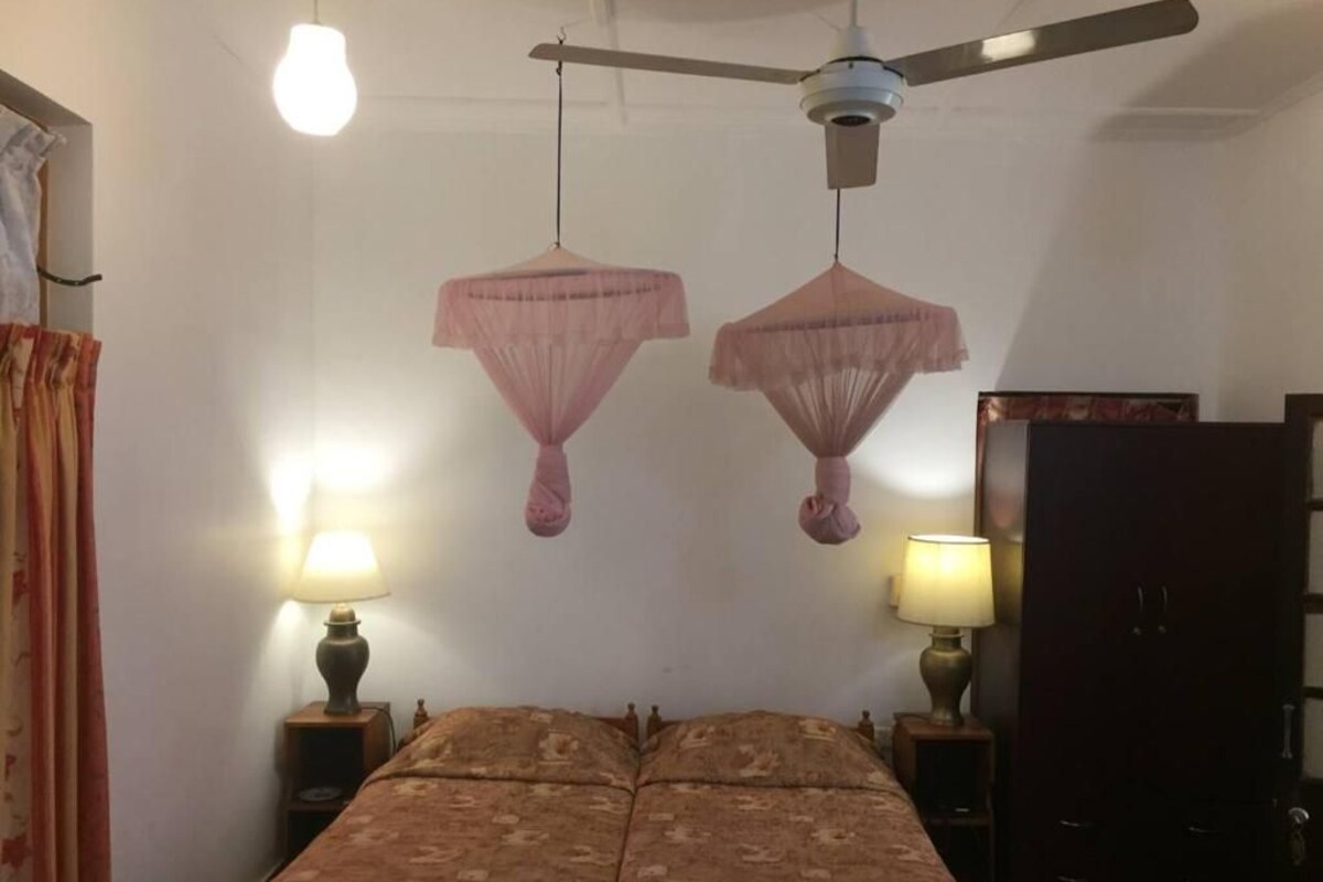 A room with a bed, two bedside lamps, a ceiling fan, and a wardrobe.