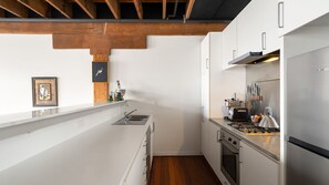 Una cucina moderna con mobili bianchi, un frigorifero in acciaio inox e un soffitto in legno.
