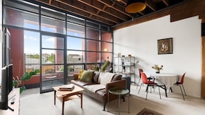 A modern living room with a leather sofa, a coffee table, and a dining area with red chairs. - Myrtle House Loft - City Views & Amazing Rooftop (Chippendale)