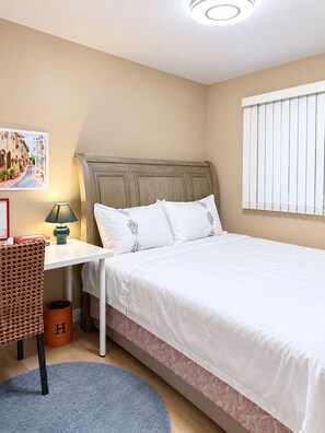 Un dormitorio ordenado con cama, mesita de noche con lámpara, una silla y un radiador fijado a la pared.