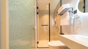 Casa de banho moderna com cabine de duche em vidro, sanita branca e toucador com espelho e porta-toalhas.
