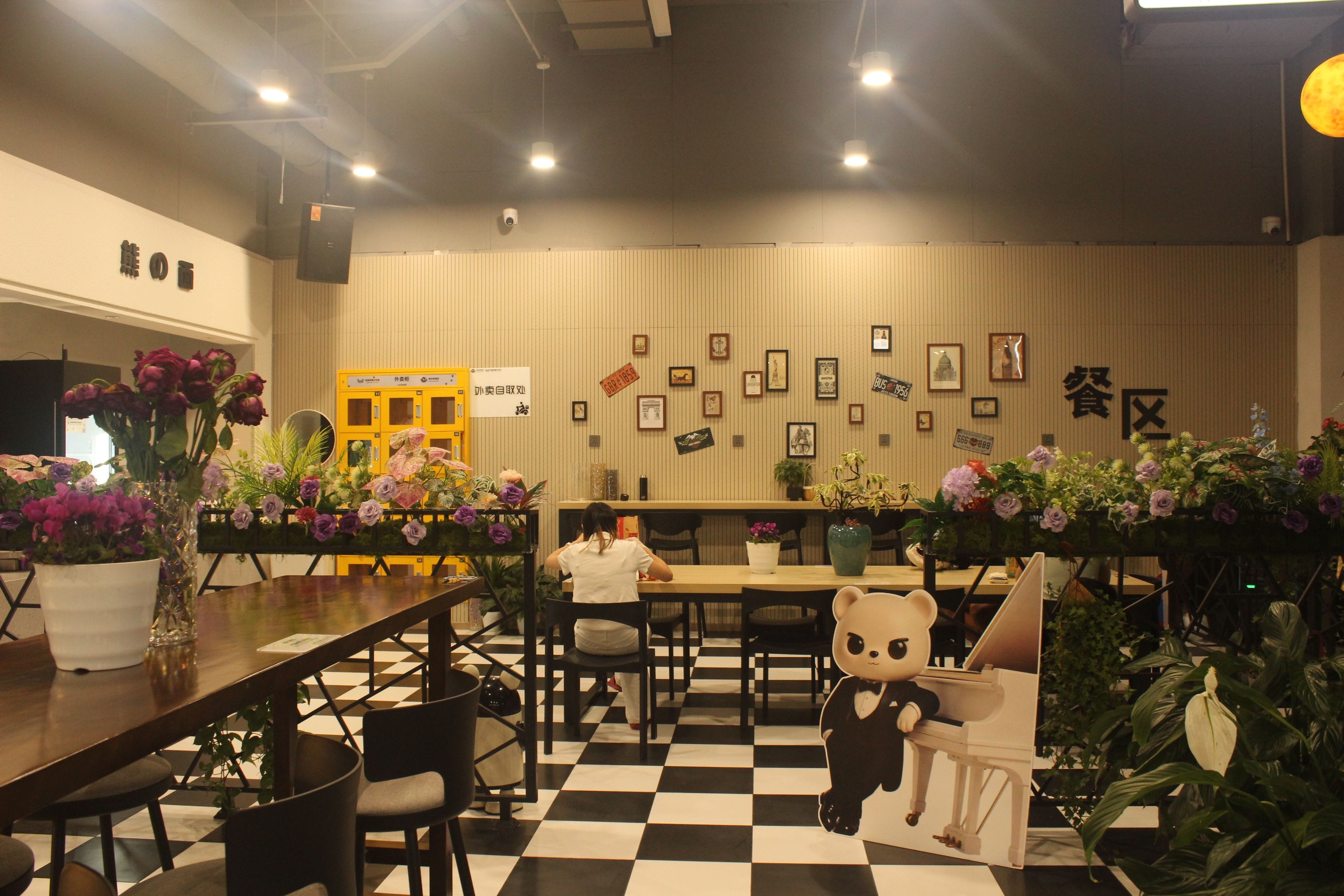 Interior de restaurante con suelo a cuadros, mesas, sillas y diversas decoraciones en las paredes, incluyendo cuadros y letreros.
