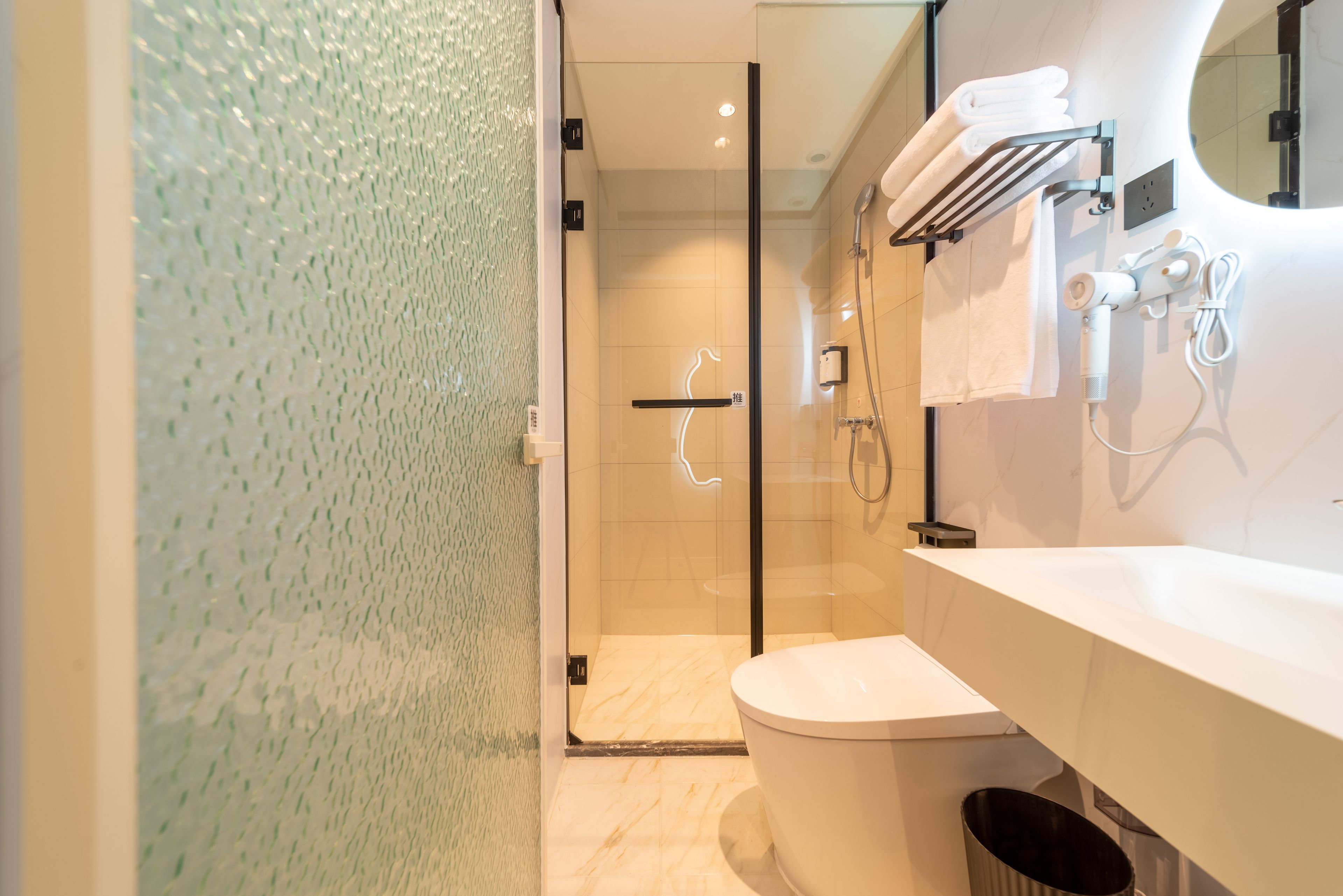 A modern bathroom with a glass shower enclosure, a white toilet, and a vanity with a mirror and towel rack.