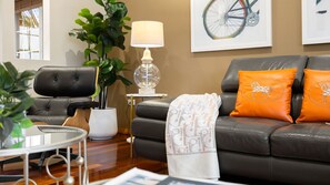 A modern living room with a leather sofa, a round table, a lamp, and a potted plant. - Yowie Bay Waters | Pool, Spa & Port Hacking Views (Yowie Bay)