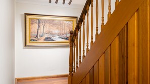 A staircase with wooden balusters and a framed painting of a forest scene on the wall. - Yowie Bay Waters | Pool, Spa & Port Hacking Views (Yowie Bay)