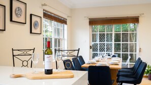 A dining area with a table set for two, a bottle of wine, and a cutting board. - Yowie Bay Waters | Pool, Spa & Port Hacking Views (Yowie Bay)