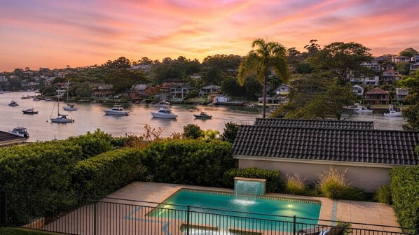 A residential area with a swimming pool, boats on the water, and houses in the background.