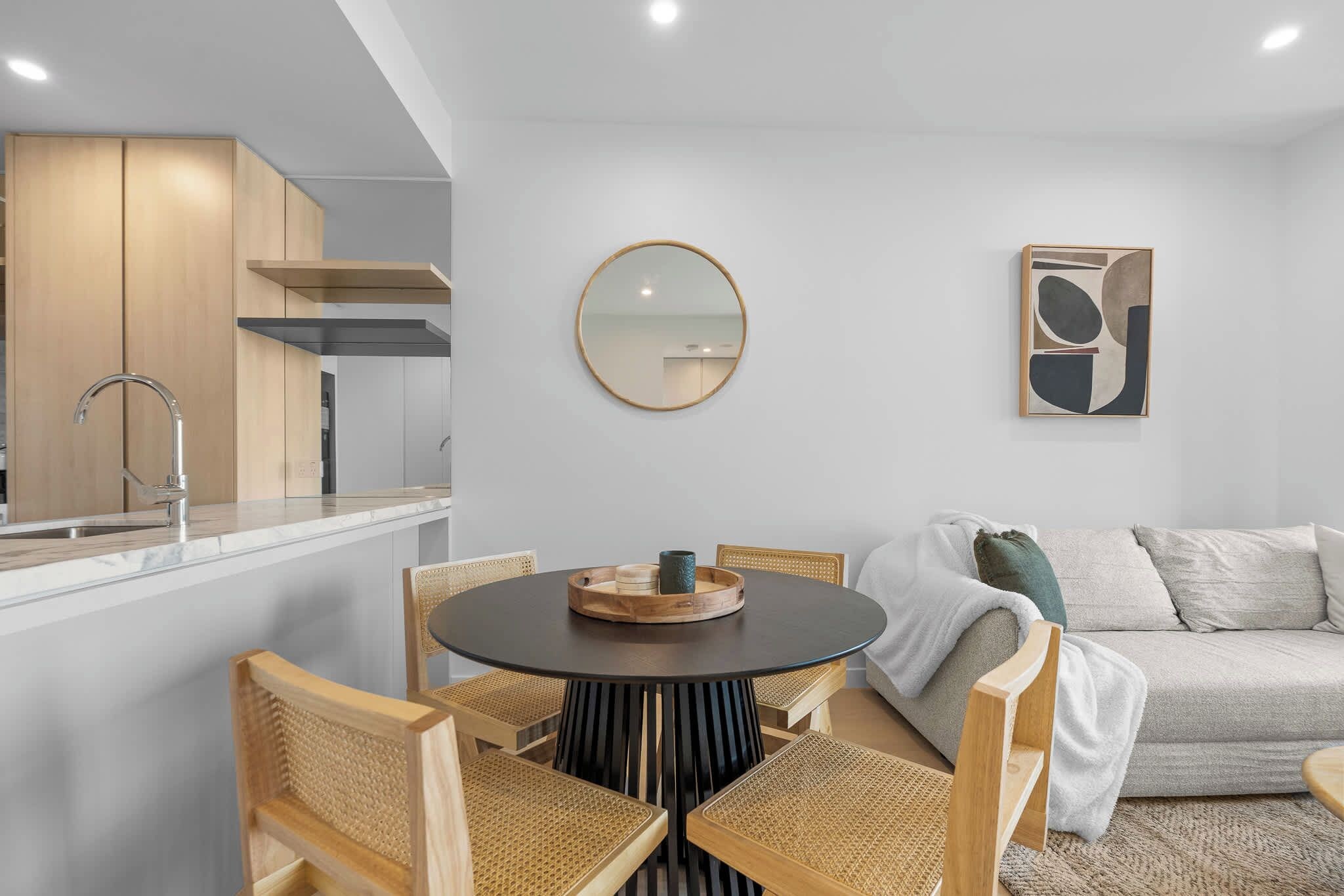 Contemporary four-seat dining area with a statement black table, rattan chairs and adjoining fully equipped kitchen in Epsilon Residence, Broadbeach.