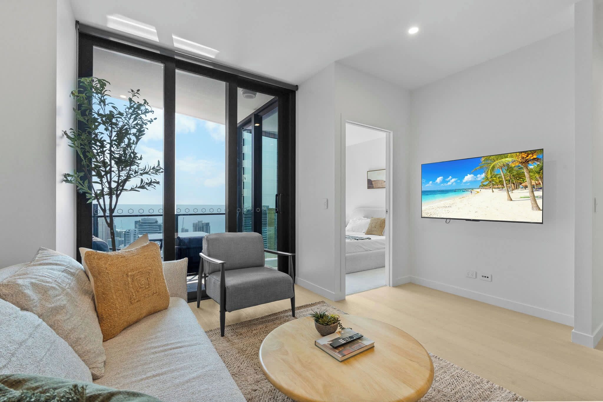 Stylish lounge with King Sofa Bed, Smart TV and floor-to-ceiling glass opening towards the private balcony and Gold Coast ocean skyline.