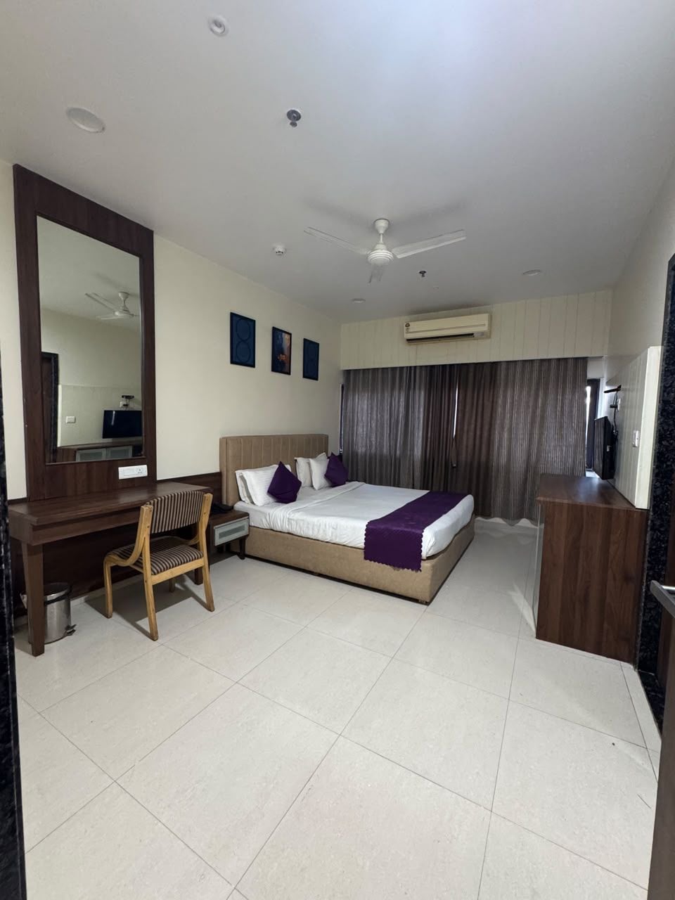 A hotel room with a bed, desk, chair, and a large mirror.