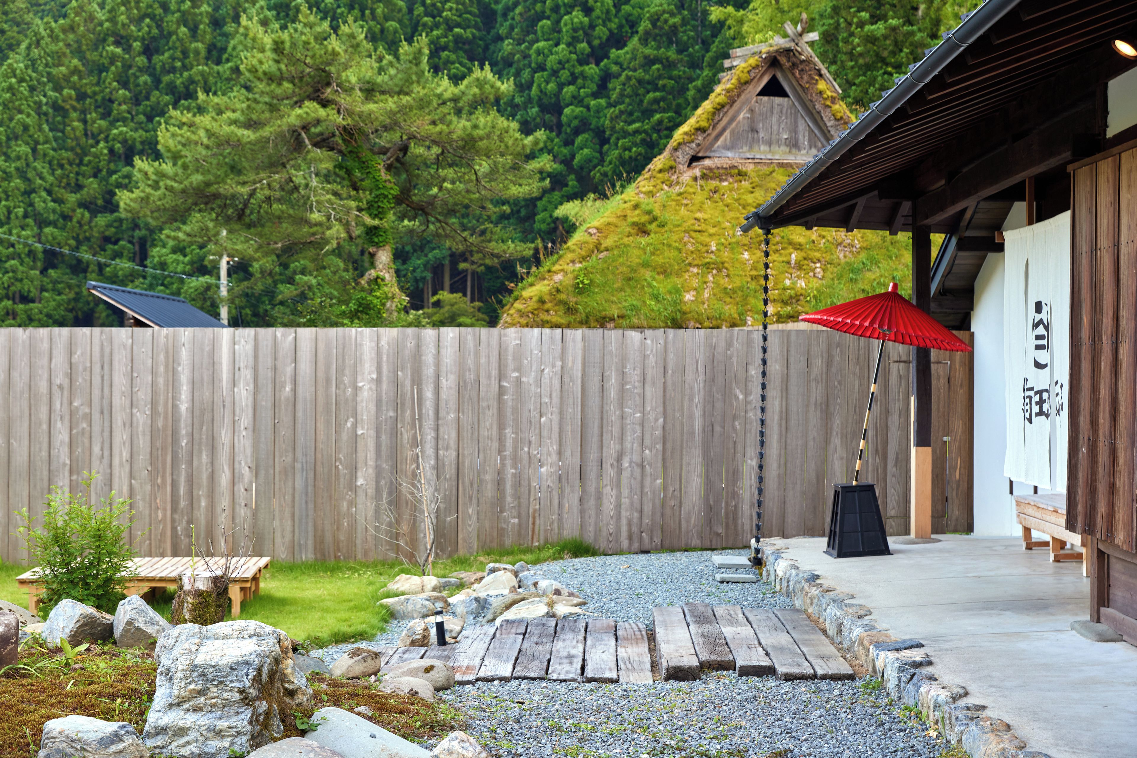 A wooden fence, a wooden deck, a red umbrella, and a building with a sloped roof.