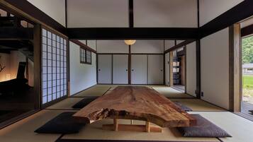 A traditional Japanese room with tatami flooring, a wooden table, sliding doors, and a view of a garden.