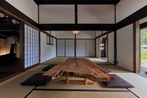 A traditional Japanese room with tatami flooring, a wooden table, sliding doors, and a view of a garden.