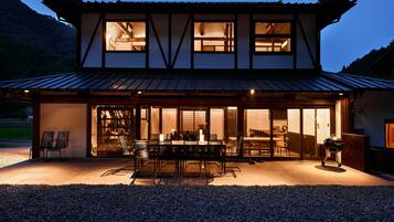 A two-story building with a traditional architectural style, featuring a dining area with tables and chairs, and a barbecue grill outside.