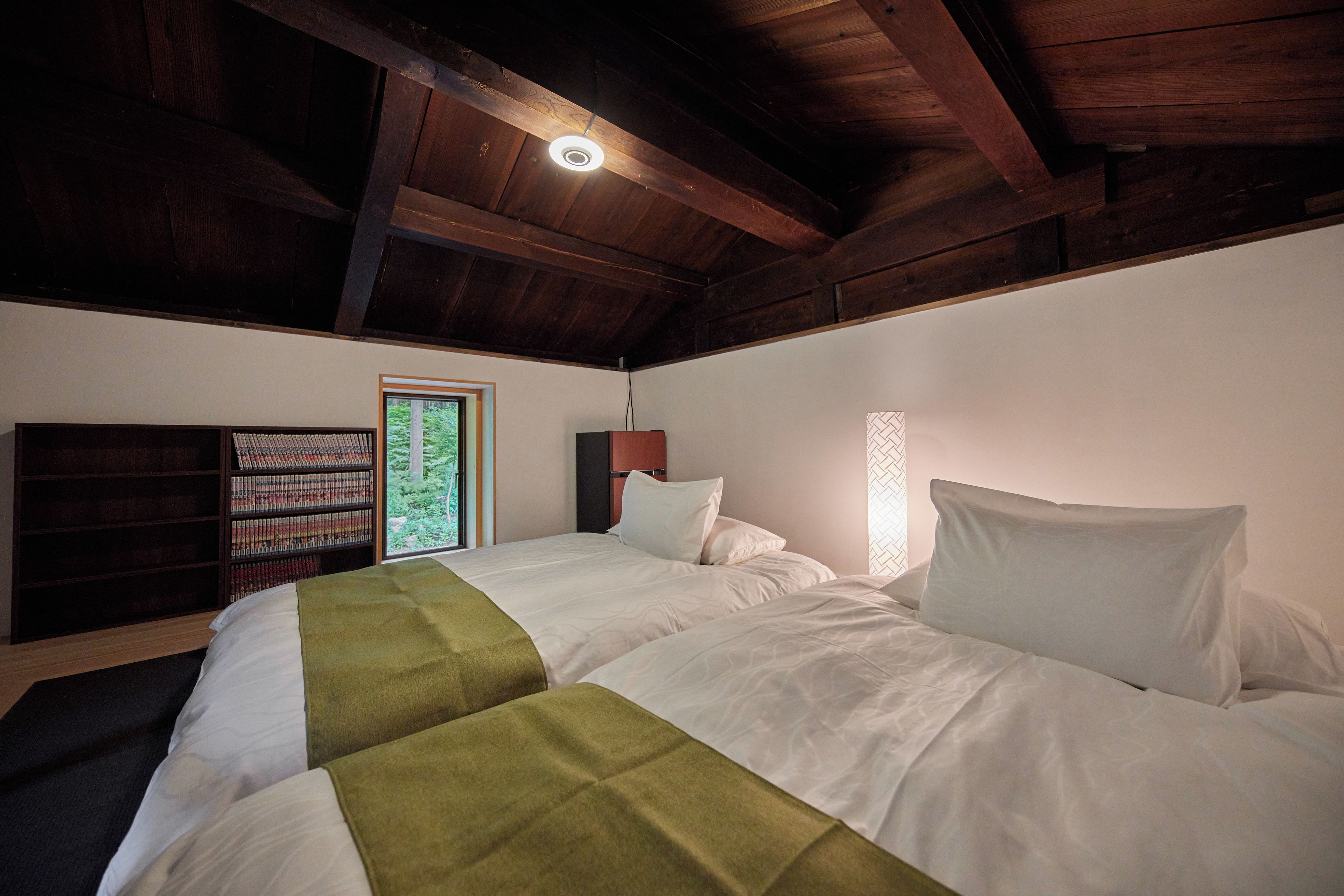 A bedroom with a bed, a bookshelf, and a window.