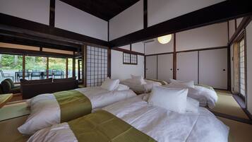 Quarto tradicional japonês com tatame, uma cama grande com várias almofadas e portas de correr.