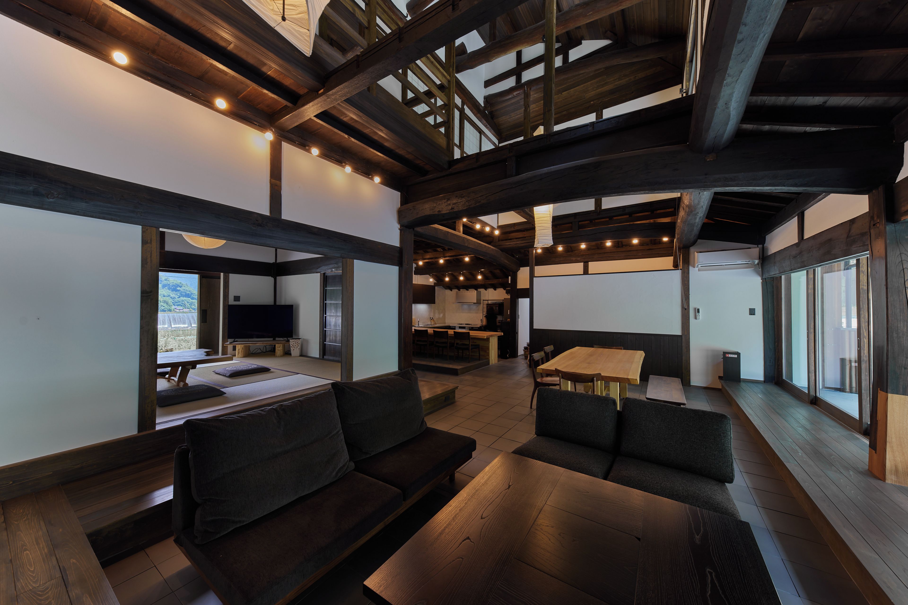 A modern interior with a high ceiling, wooden beams, and a dining area with a large table and chairs.